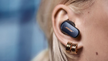 A close-up shot of a woman's ear with earrings wearing the Bose QuietComfort Earbuds II in Eclipse Grey.