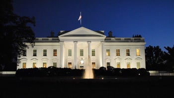 The facade of the White House at night, shot from the ground.