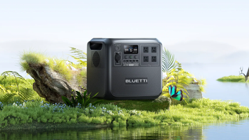 Bluetti AC180 power station displayed in a lush, green outdoor setting with rocks, plants, a lake, and a butterfly.