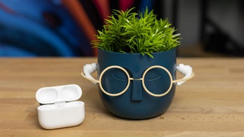 AirPods Pro 2 resting on a fun plant pot with the charging case placed beside it on a wooden table.