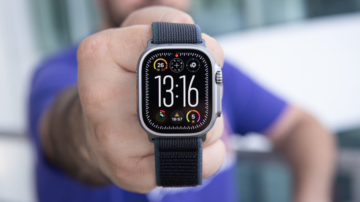 A close-up of the Apple Watch Ultra 2 being held on a blurred background. The screen is on and shows different metrics.