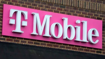 A magenta sign with the T-Mobile logo in white sits on top a brick T-Mobile store.