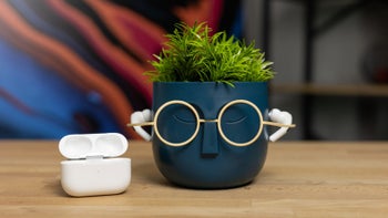 AirPods Pro 2 displayed on a human-like plant pot, with the charging case next to them, placed on a table.