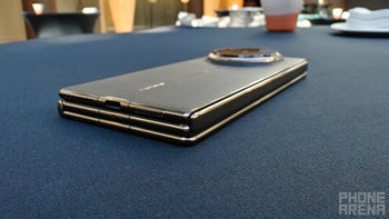 Huawei Mate XT in black color displayed in its folded state, resting on a table.