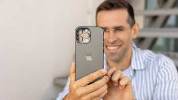 PhoneArena's Vic is smiling as he looks at the iPhone 16 Pro Max display while the rear panel is displayed to the viewer.