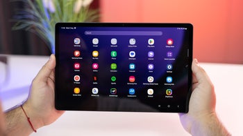 A close-up of a person holding the Galaxy Tab S9. The tablet's screen is turned on and showcases various apps.