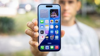 PhoneArena's Vic holds up an iPhone 16 base model with the display facing the camera.