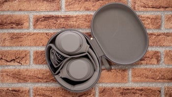 A pair of Sony WH-1000XM4 headphones placed inside their carrying case that rests against a textured brick wall background.