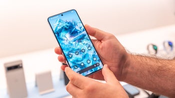 A close-up of a person holding the Pixel 8 Pro. The phone's display is turned on and shows the home screen.