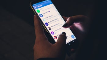 A pair of hands holding a phone with the Telegram app on it, in a poor-lit room.