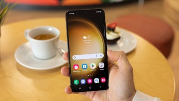 A Galaxy phone held in a person's hand in a coffee shop.