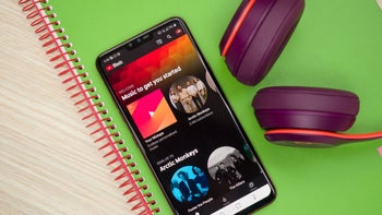 YouTube Music on a phone with headphones next to it on a colorful table.