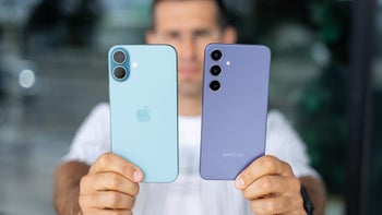 A person's hand holding an iPhone 16 in blue and a Galaxy S24 in purple side-by-side.