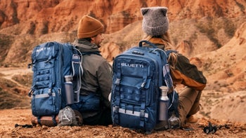 Two people sitting on the ground, wearing the Bluetti Handsfree Backpack on their backs, while enjoying the scenery.