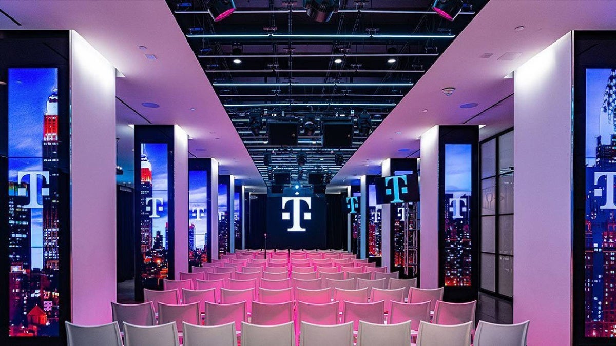 A projection room for T-Mobile shows the T-Mobile logo on the screen and on the windows, and rows of theater-style chairs.