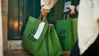 Uber Eats delivery person holding food bags and a smartphone.