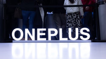 Letters spelling "OnePlus" are seen on a table in white and are reflecting off of it.