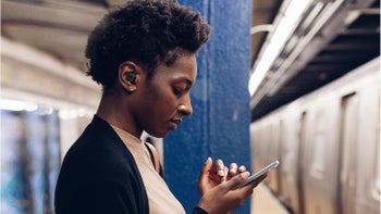 A woman wearing Galaxy Buds FE, listening to music while waiting at the subway.