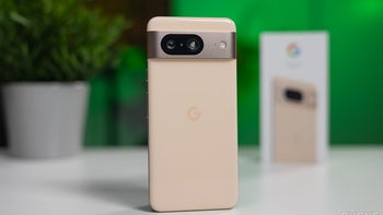 A Google Pixel 8 positioned in the foreground on a surface with a blurred product box in the background against a bright green backdrop