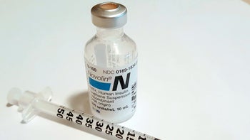 A vial of long acting insulin is seen on a table next to an insulin syringe.