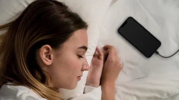 A woman is sleeping with her head on a pillow and her iPhone charging right beside her.