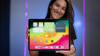 Smiling woman holds the 13-inch iPad Air M2 (2024) with a turned-on screen against a blue and purple background.