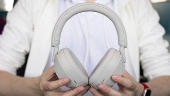 A close-up of a person with white clothes holding the Sony WH-1000XM5 in Silver.