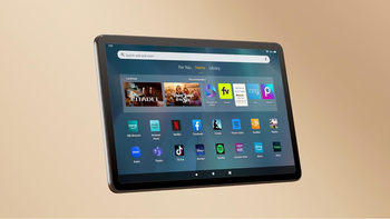 Amazon Fire Max 11, with a turned-on display, is set against a tan-brown background and showcases different app icons.