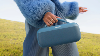 A person wearing a blue fuzzy jacket holding a Bose SoundLink Max speaker outdoors.