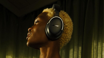 A person wearing the Bose QuietComfort Ultra headphones with a relaxed expression, side profile against a dark background.