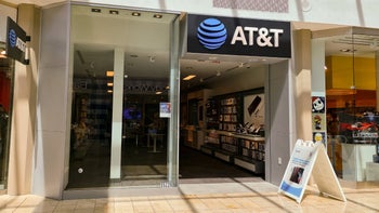 The front of an AT&T Store in a shopping mall is shown with the AT&T logo and wordmark above a big picture window.