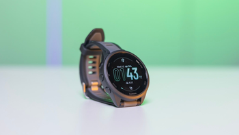 Garmin Forerunner 165 is placed on a white table against a green background. The watch's screen is on, showing the time.