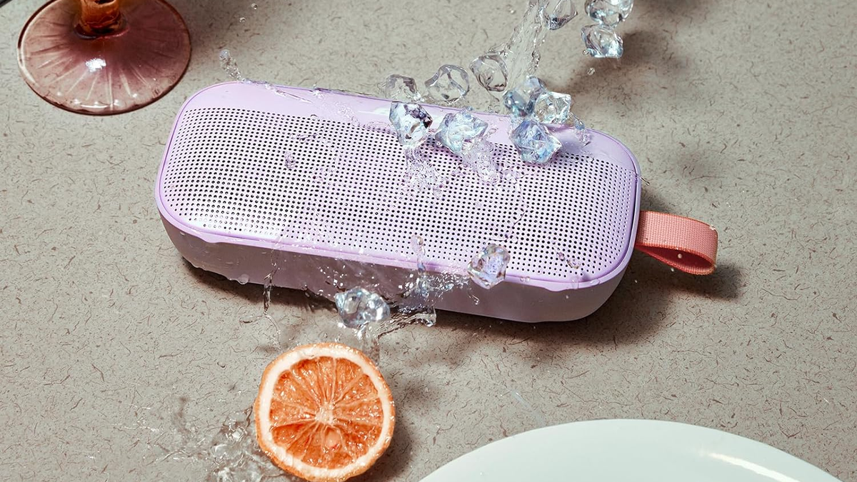 Bose SounLink Flex in Chilled Lilac, shown with water splashes and an orange on a beige surface.