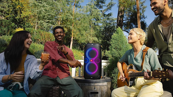 A group of friends enjoying music outdoors with a JBL PartyBox 110 speaker, featuring vibrant LED light effects.