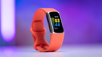 A red Fitbit Charge 6 fitness tracker displayed on a white surface with a blurred blue and purple background.