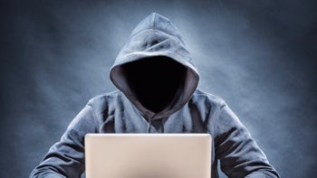 A mysterious hooded figure whose face is blacked out is looking at stolen personal data from a smartphone on a laptop.