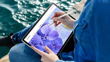 A woman has placed the Galaxy Tab S9 FE+ on her lap, editing an image of purple flowers with the S Pen.