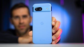 A Pixel phone placed on a table held by a person in the background.