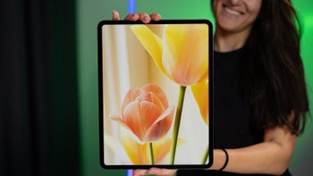 A smiling woman holds the 13-inch iPad Pro M4, displaying a vibrant image of tulips.