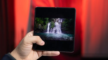 A person holds the OnePlus Open against a blurred red background, showcasing its main display.