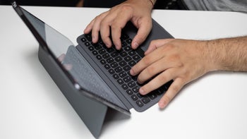 Hands typing on the OnePlus Pad 2 connected to its proprietary smart keyboard accessory on a white table.