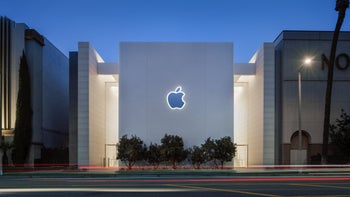 The Apple logo appears on an Apple Store at dusk with the lights on.