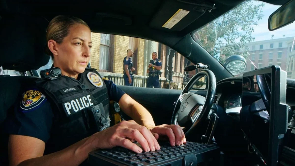 A poicewoman is typing on the laptop computer inside her patrol car.