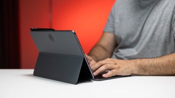 A person typing on a OnePlus Pad 2 with a keyboard accessory, set against a red background.