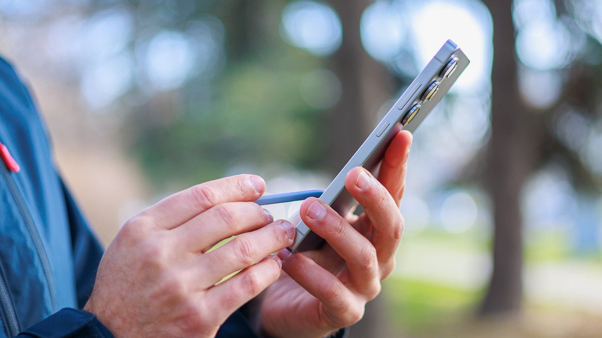 Side view of Galaxy S25 Ultra held in hand, other hand using the S Pen to write something on the screen