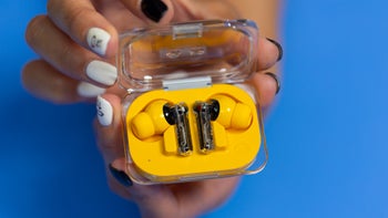 A close-up of hands holding the Nothing Ear (a) in their opened charging case, showing their minimalist design.