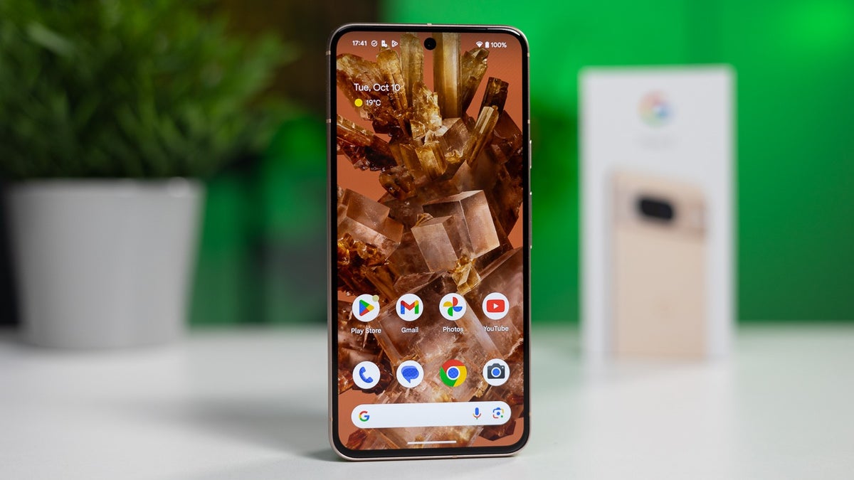 A Pixel 8 phone is placed on a white table against a blurred background, with its retail box visible on the background.