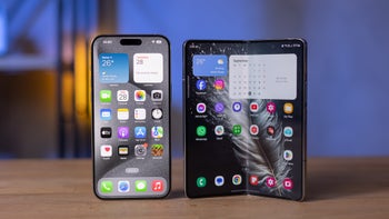 iPhone 15 Pro Max next to Galaxy Z Fold 5 placed side-by-side on a wooden surface.