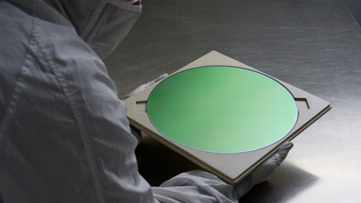 Employee at Apple supplier examines a silicon wafer used to make integrated circuits.