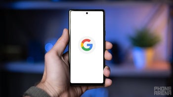 An Android phone is held in the left hand while the iconic Google "G" logo is on the display.